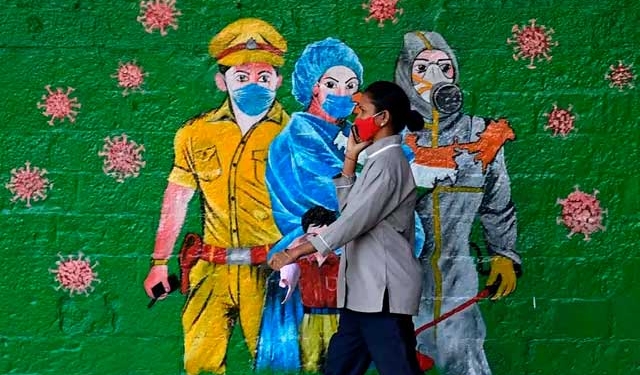 Una mujer con mascarilla frente a un mural en India durante la pandemia de coronavirus - Ashish Vaishnav/SOPA Images