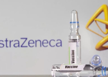 Un tubo de ensayo etiquetado con la vacuna se ve delante del logo de AstraZeneca | Foto Reuters