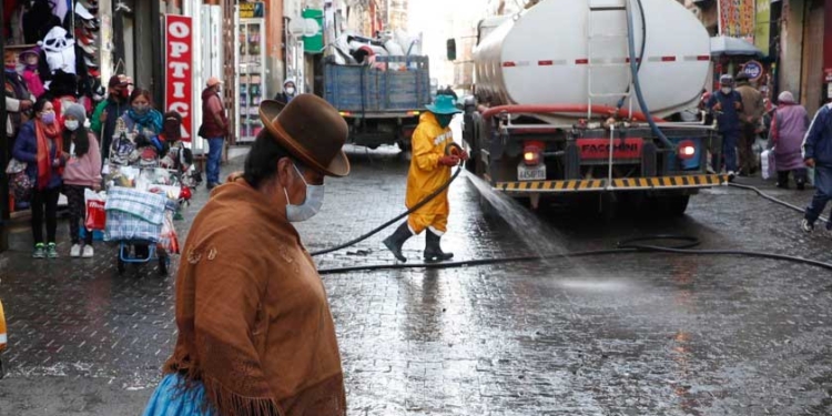 Una mujer pasa junto a trabajadores de la ciudad que desinfectan la calle en medio de la pandemia de coronavirus en La Paz, Bolivia | Foto: Juan Karita (ASSOCIATED PRESS)