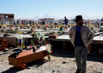 Un hombre junto al ataúd de un pariente en un cementerio en las afueras de La Paz. Credit...David Mercado/Reuters