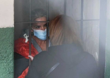 De pie tras las rejas, la expresidenta interina de Bolivia, Jeanine Añez, habla con una mujer