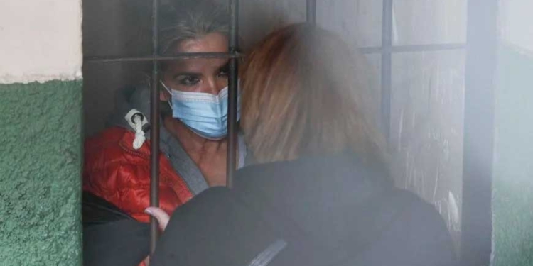 De pie tras las rejas, la expresidenta interina de Bolivia, Jeanine Añez, habla con una mujer